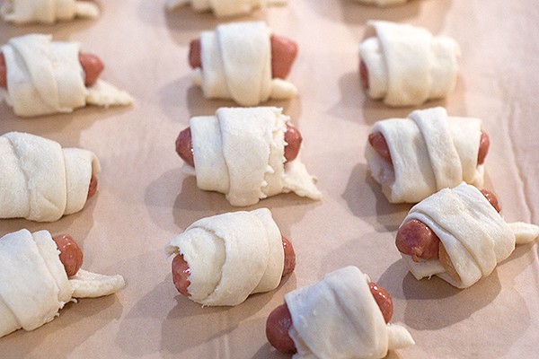 Rolls of crescent dough, sausages, and pineapple on a baking sheet.