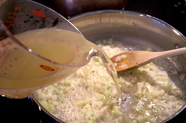 Adding chicken stock to the skillet with cooked onions, celery, and flour.