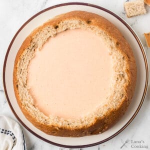 Round loaf of bread hollowed out and filled with creamy beer cheese dip, placed on a white plate.