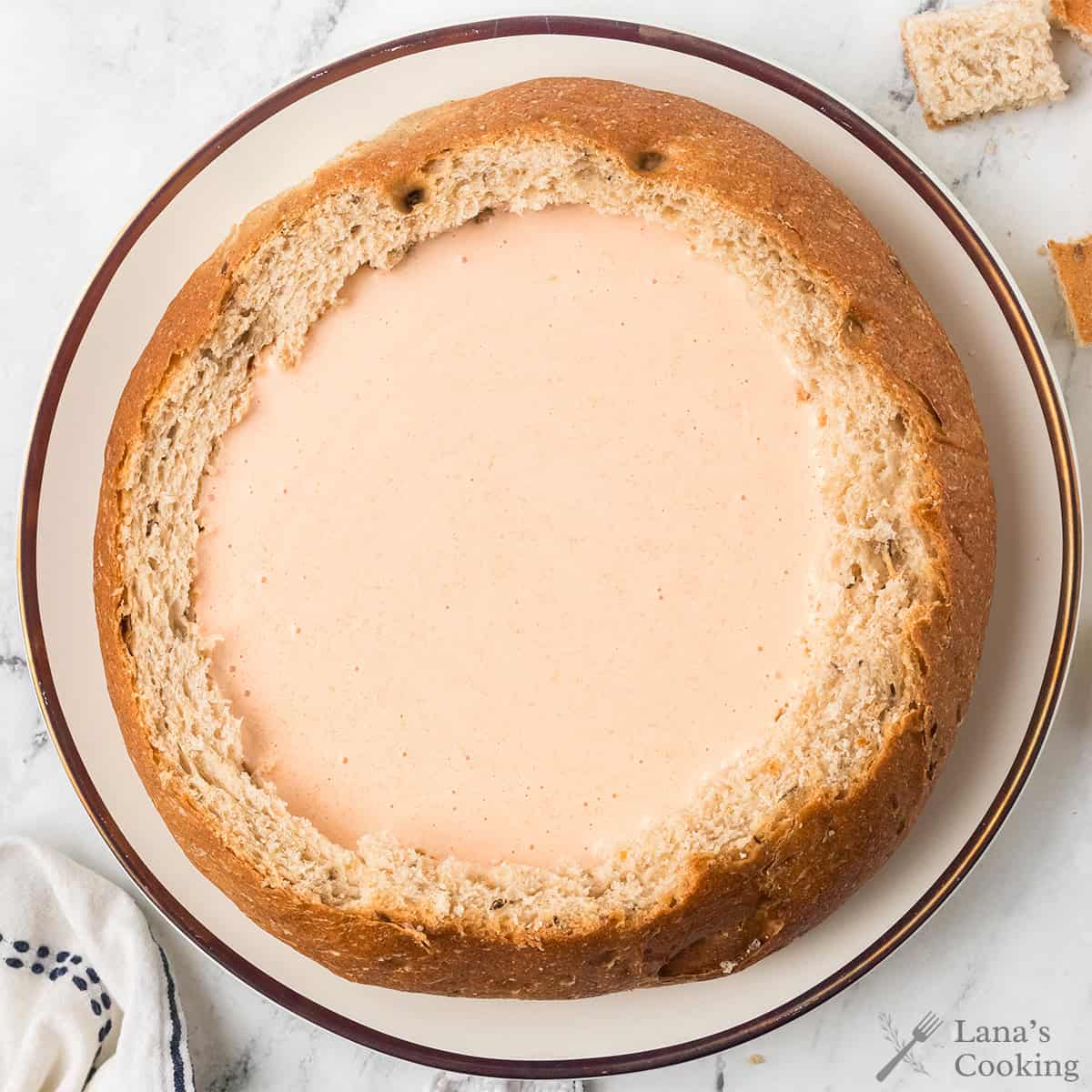 Round loaf of bread hollowed out and filled with creamy beer cheese dip, placed on a white plate.