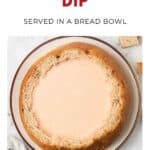 A round bread bowl filled with creamy beer cheese dip, served on a plate with bread pieces nearby.