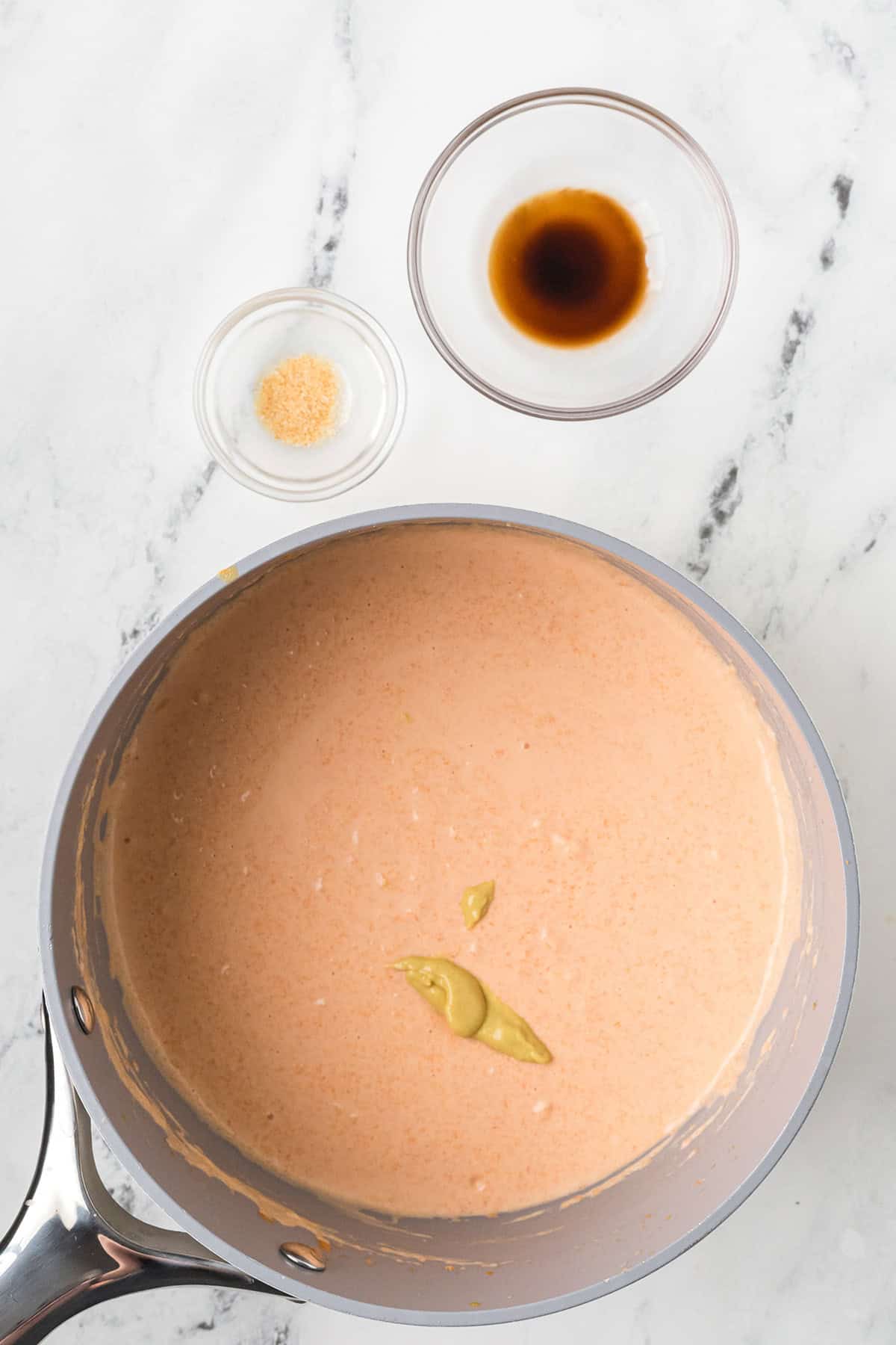 A saucepan of creamy beer cheese dip with mustard on top; two small bowls hold spices and a dark liquid.
