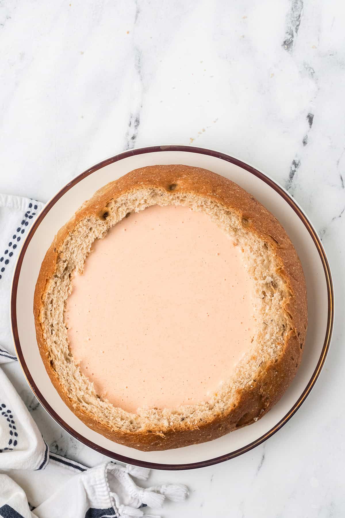 Round loaf of bread with the center hollowed and filled with dip, on a plate.