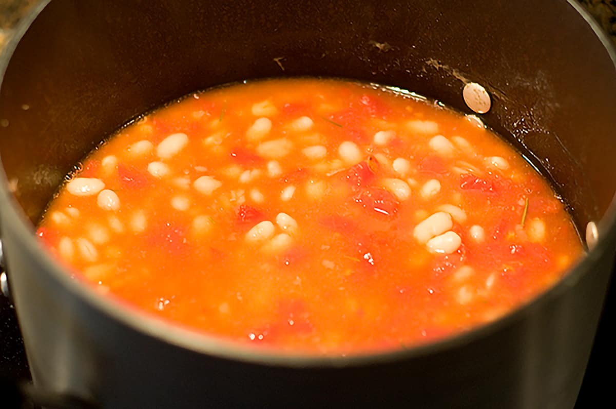 Pot of beans with final ingredients, including tomatoes, added.