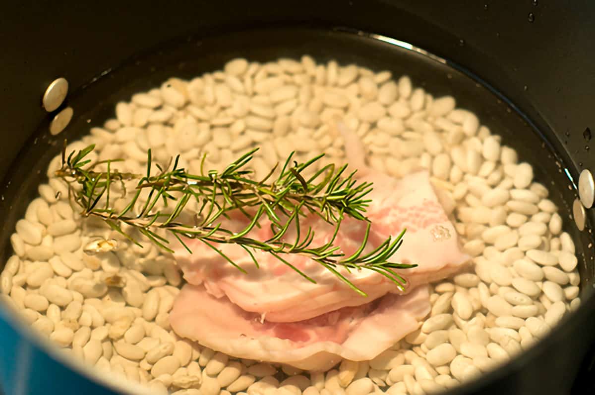 Beans in a pot with pork and fresh rosemary on top