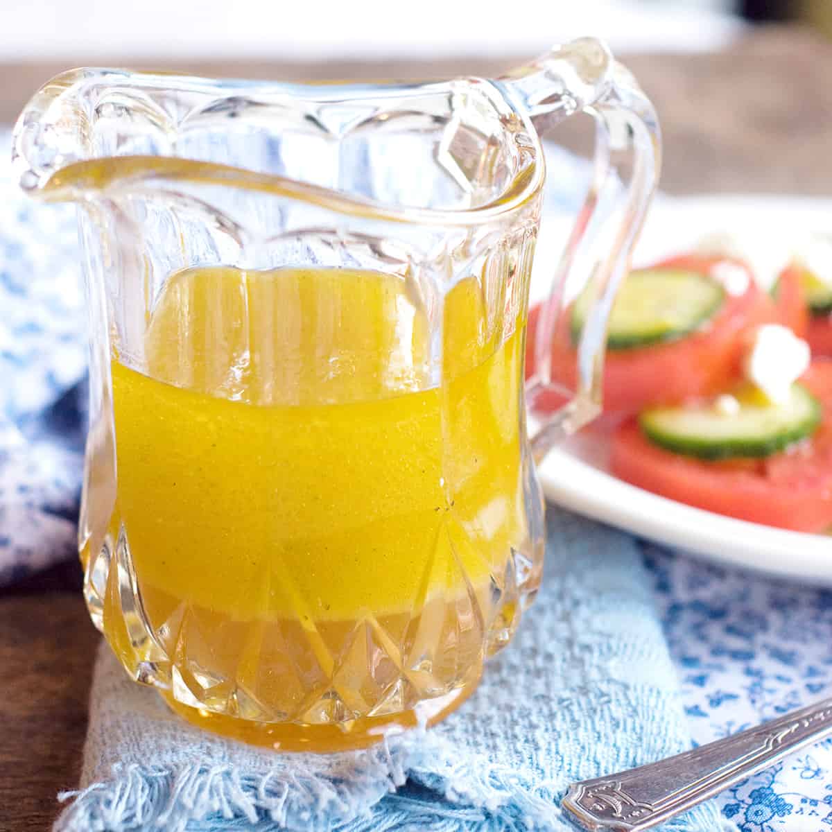 A small glass pitcher filled with lemon vinaigrette; salad in the background.