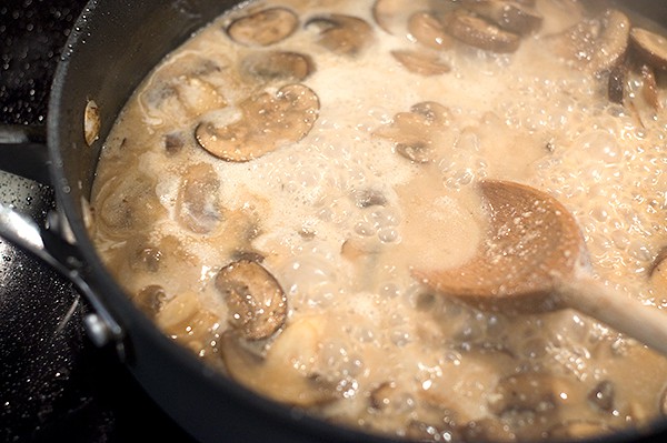 Adding Parmesan cheese to the mushroom sauce mixture in a skillet.