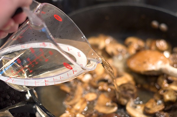 Adding white wine and chicken broth to mushrooms in skillet.