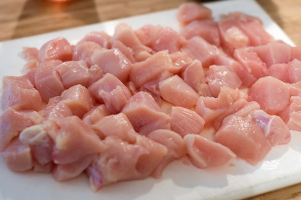 Chicken breast cut into 1-inch pieces on a cutting board.