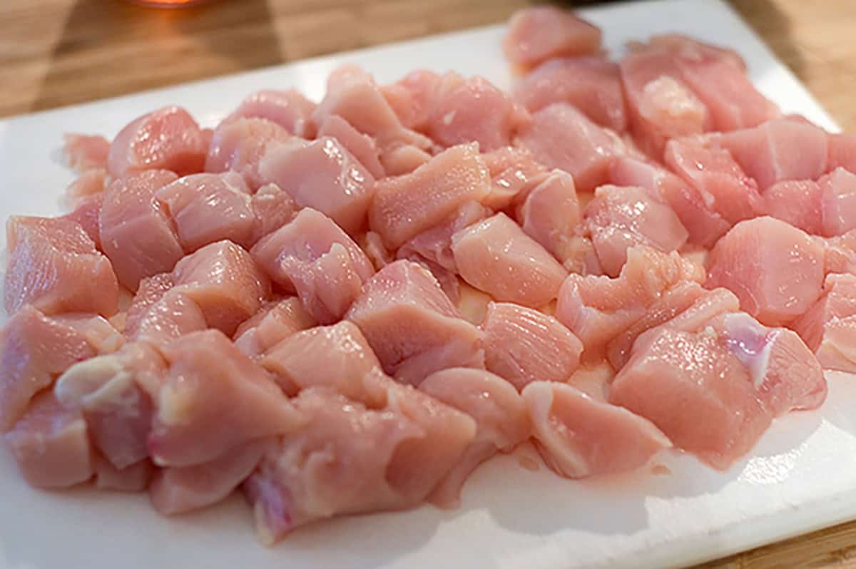 Chicken breast cut into 1-inch pieces on a plastic cutting board.