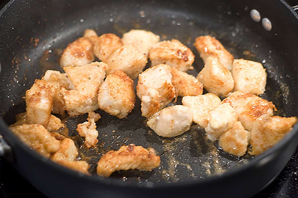 Chicken pieces cooking in a skillet.