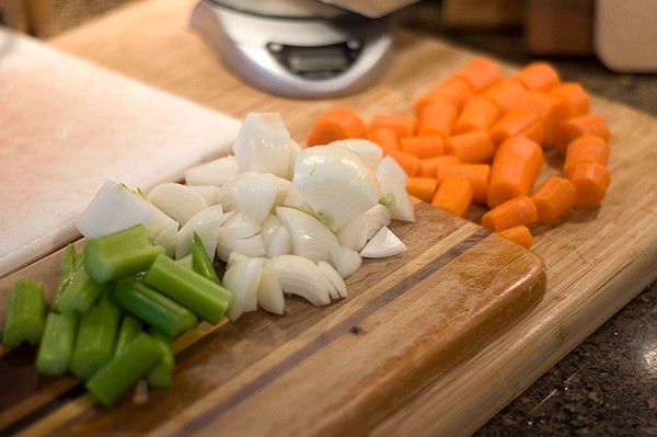 Prepped celery, onion, and carrots on a cutting board.