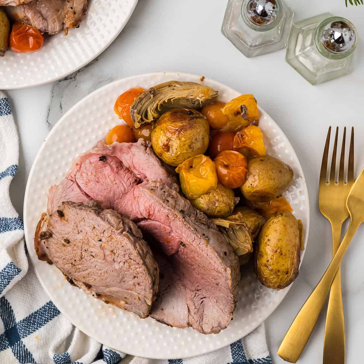 Slices of lamb surrounded by roasted vegetables.