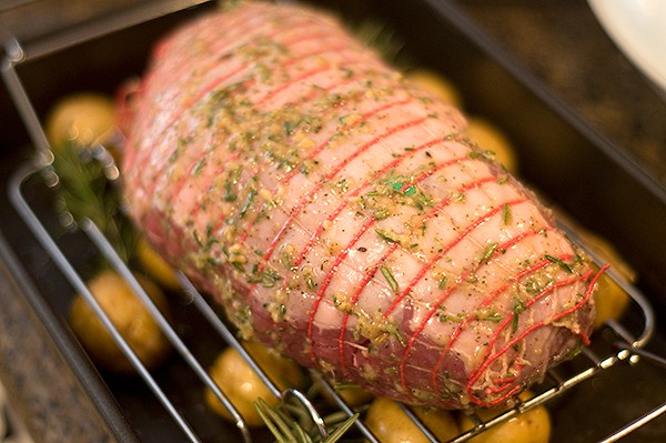 Leg of lamb on a roasting rack above potatoes in a baking pan.