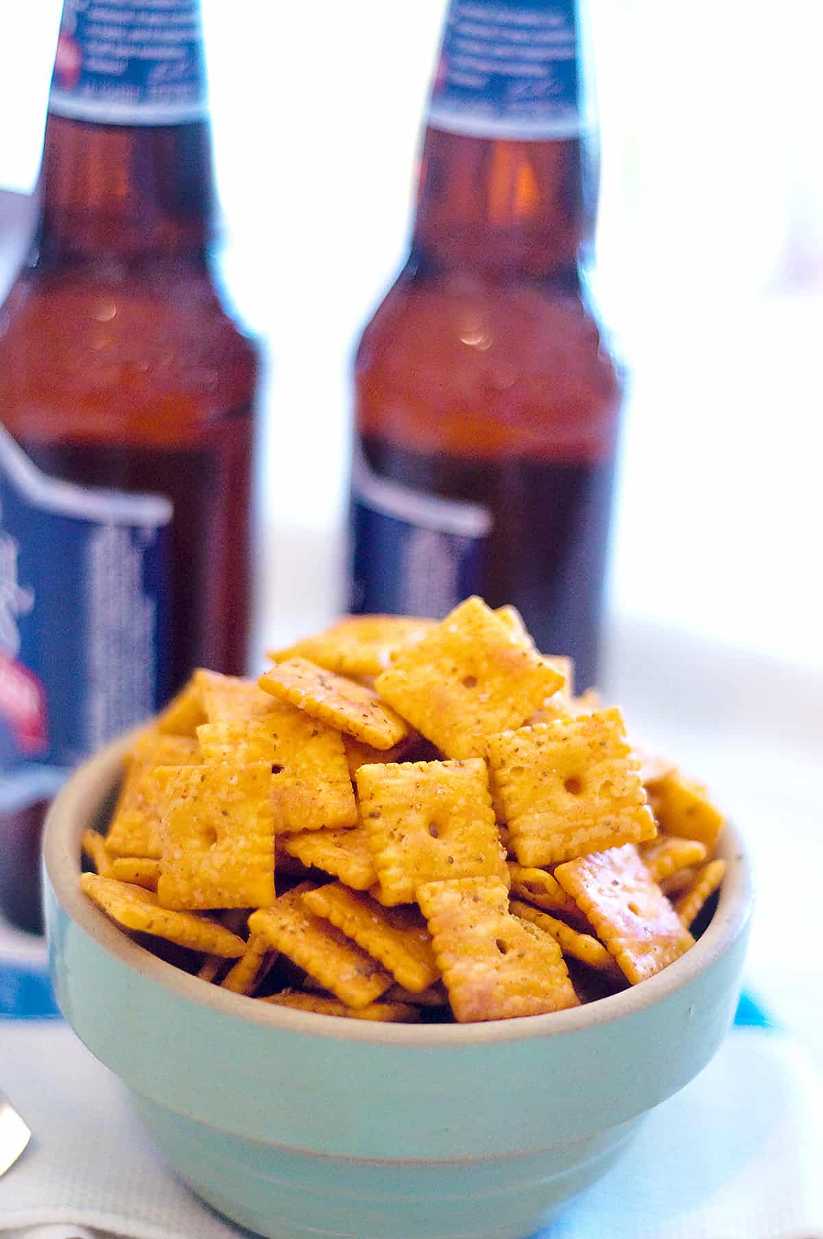 Cheese crackers in a vintage serving bowl with two bottles in the background.