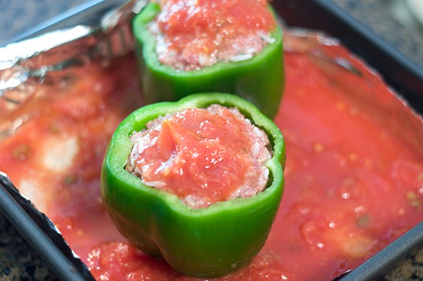 Stuffed peppers in baking pan with tomato mixture.