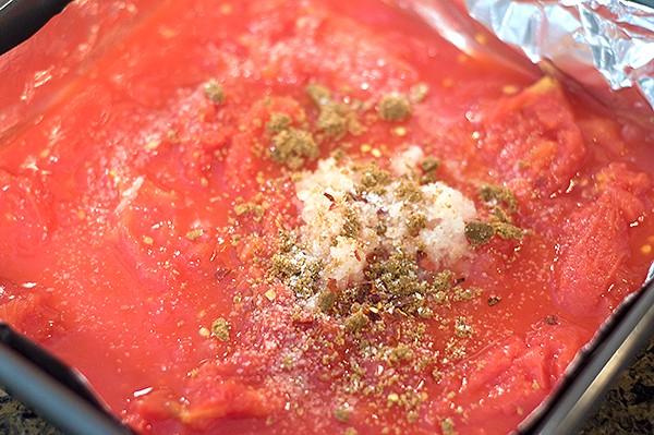 Tomatoes, onion, and seasonings in a baking pan.