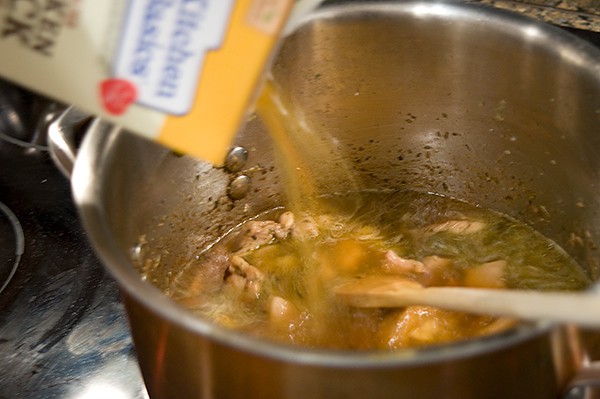 Adding chicken stock to the cooked chicken.