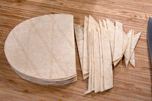 Cutting tortillas into strips on a cutting board.