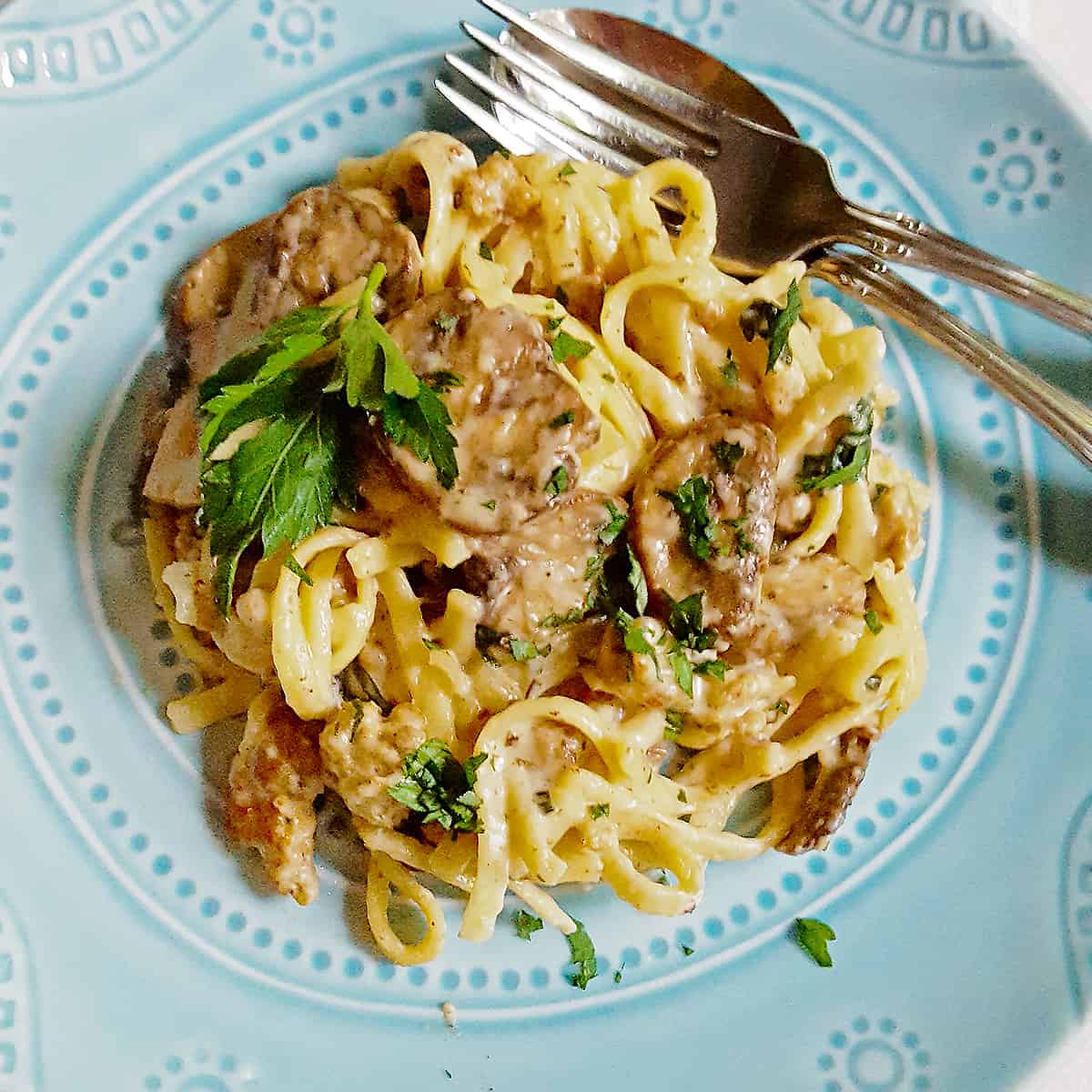 A serving of Italian sausage alfredo on a blue plate.