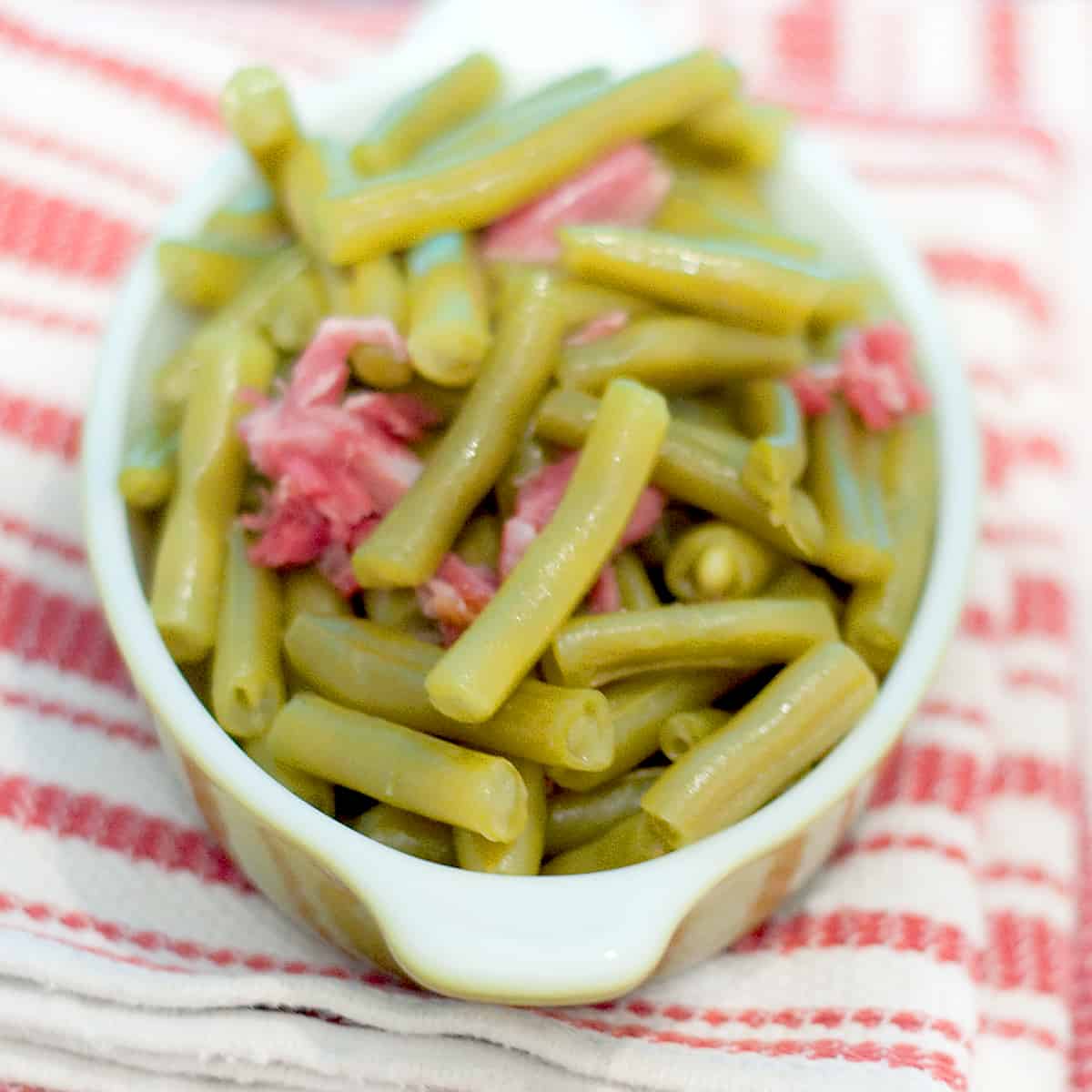 Old Fashioned Southern Green Beans with smoky bacon in a small bowl resting on a kitchen towel.