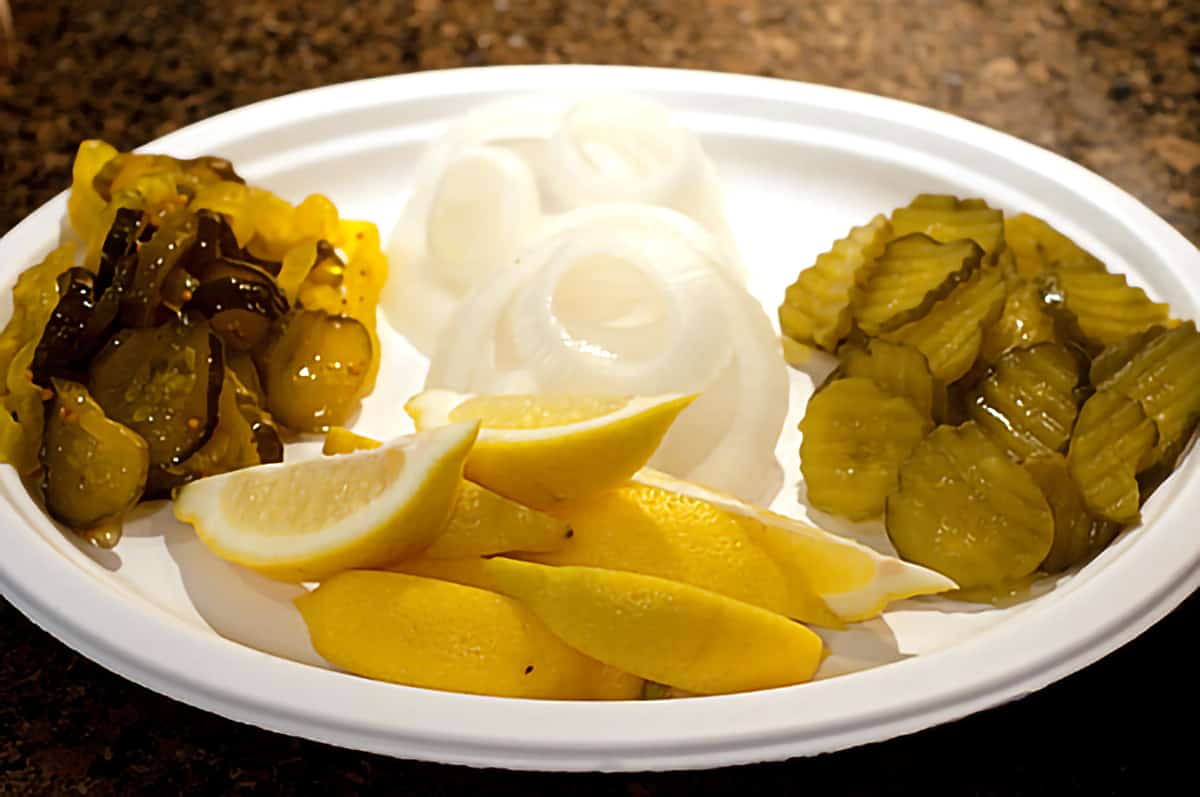 A plate of onion slices, dill pickles, lemon wedges, and sweet pickles.