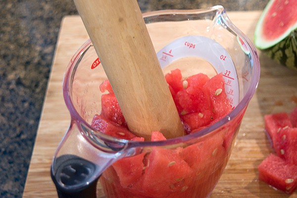 Using a muddler to crush the watermelon in a measuring cup.