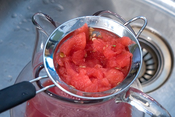 Straining watermelon juice into a pitcher.