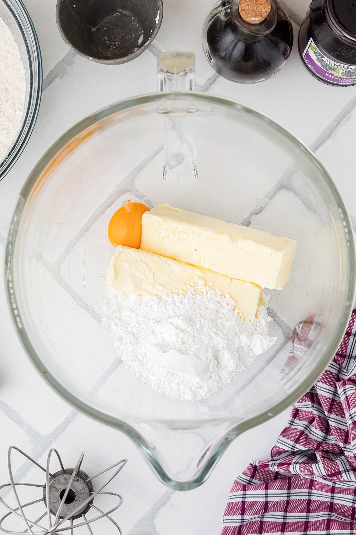 A glass bowl with butter, powdered sugar, and an egg yolk, surrounded by baking ingredients and utensils.
