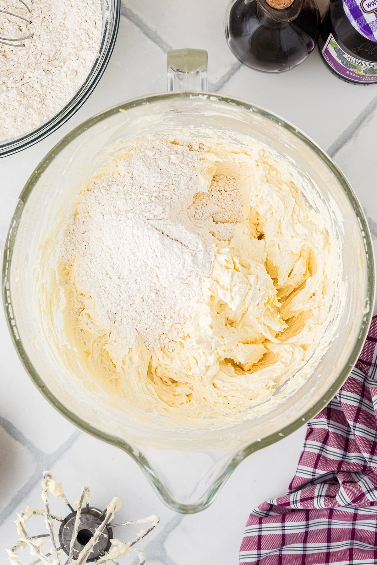 A stand mixer bowl with creamed butter and sugar, partially mixed with flour, sits on a countertop.