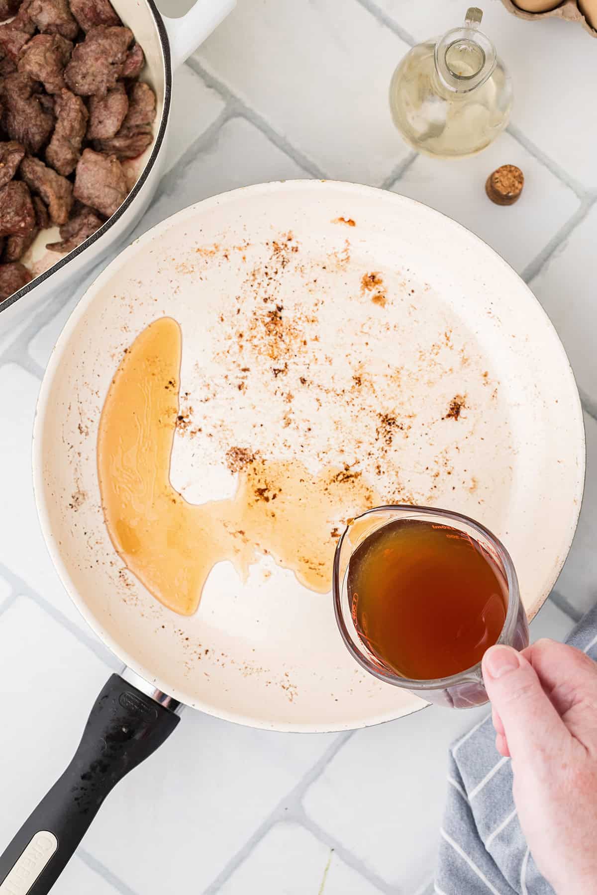 Adding beef stock to the skillet.