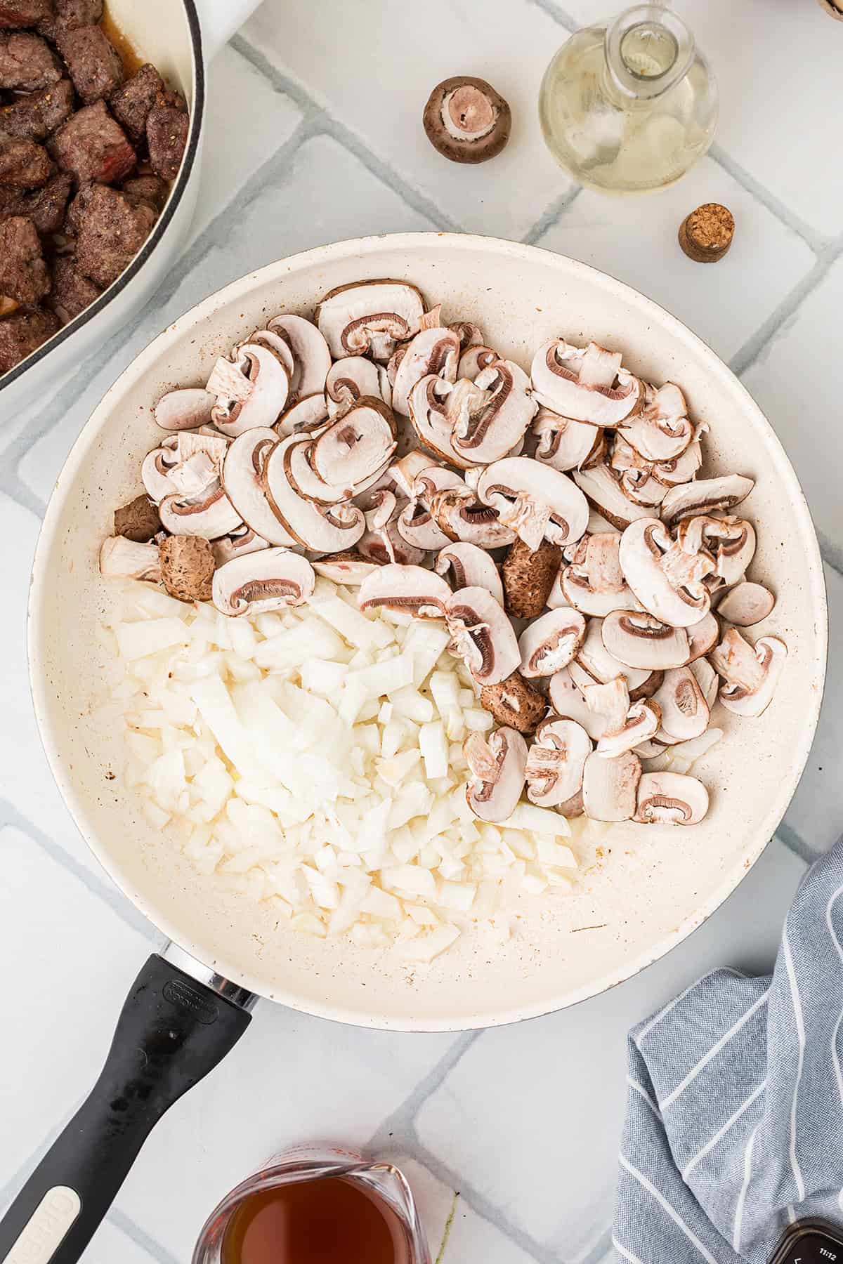 Mushrooms and onions cooking in a frying pan.