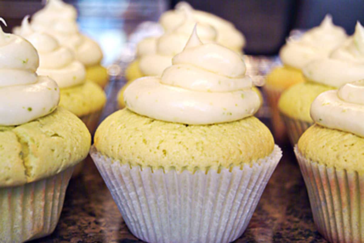 Lemon cupcakes with swirls of white frosting, arranged in rows on a countertop.