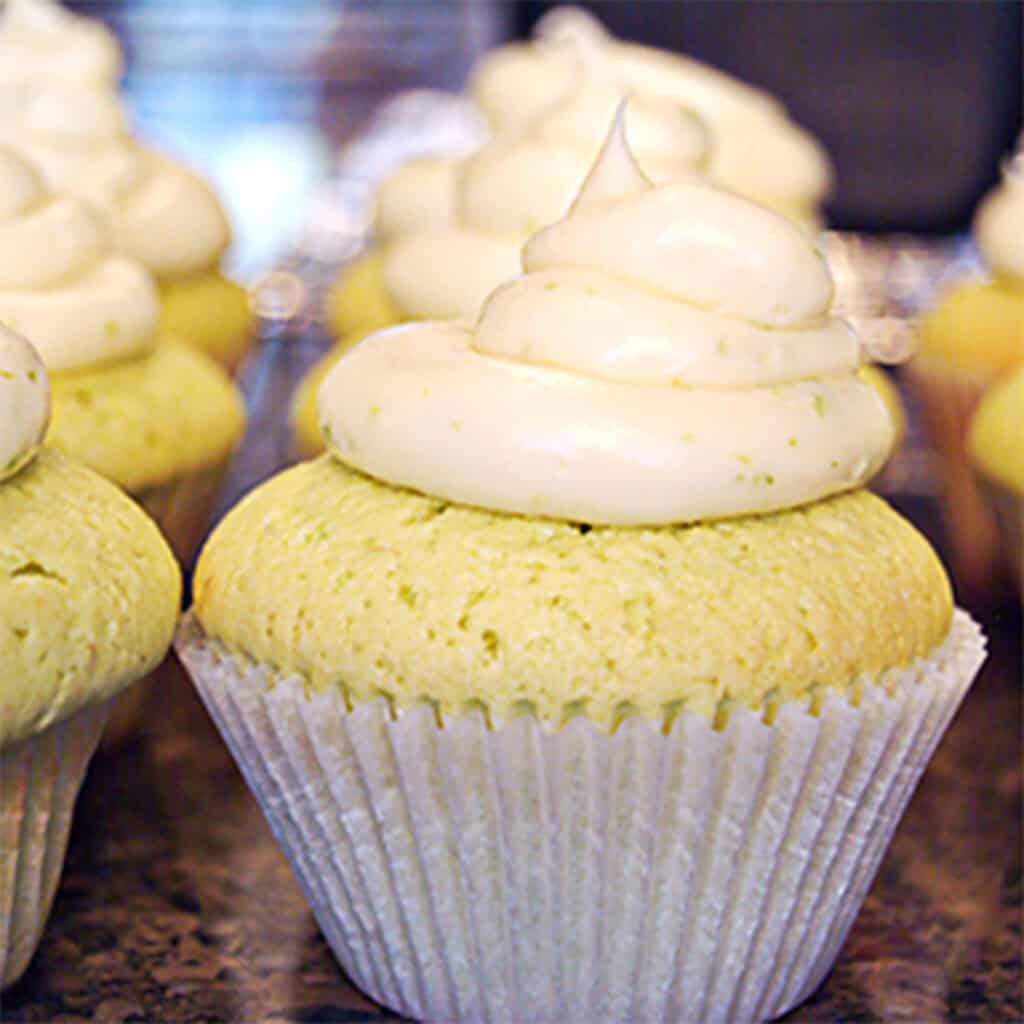A close-up of cupcakes with white swirled frosting in paper liners on a countertop.