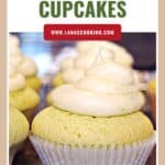 Lime cupcake with creamy frosting in a white liner, surrounded by similar cupcakes on a counter.