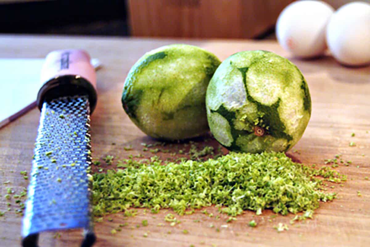Two limes, a grater, and a small pile of lime zest on a wooden surface.