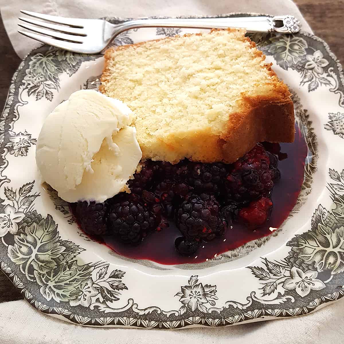 A slice of pound cake on a serving plate with ice cream and berry compote.