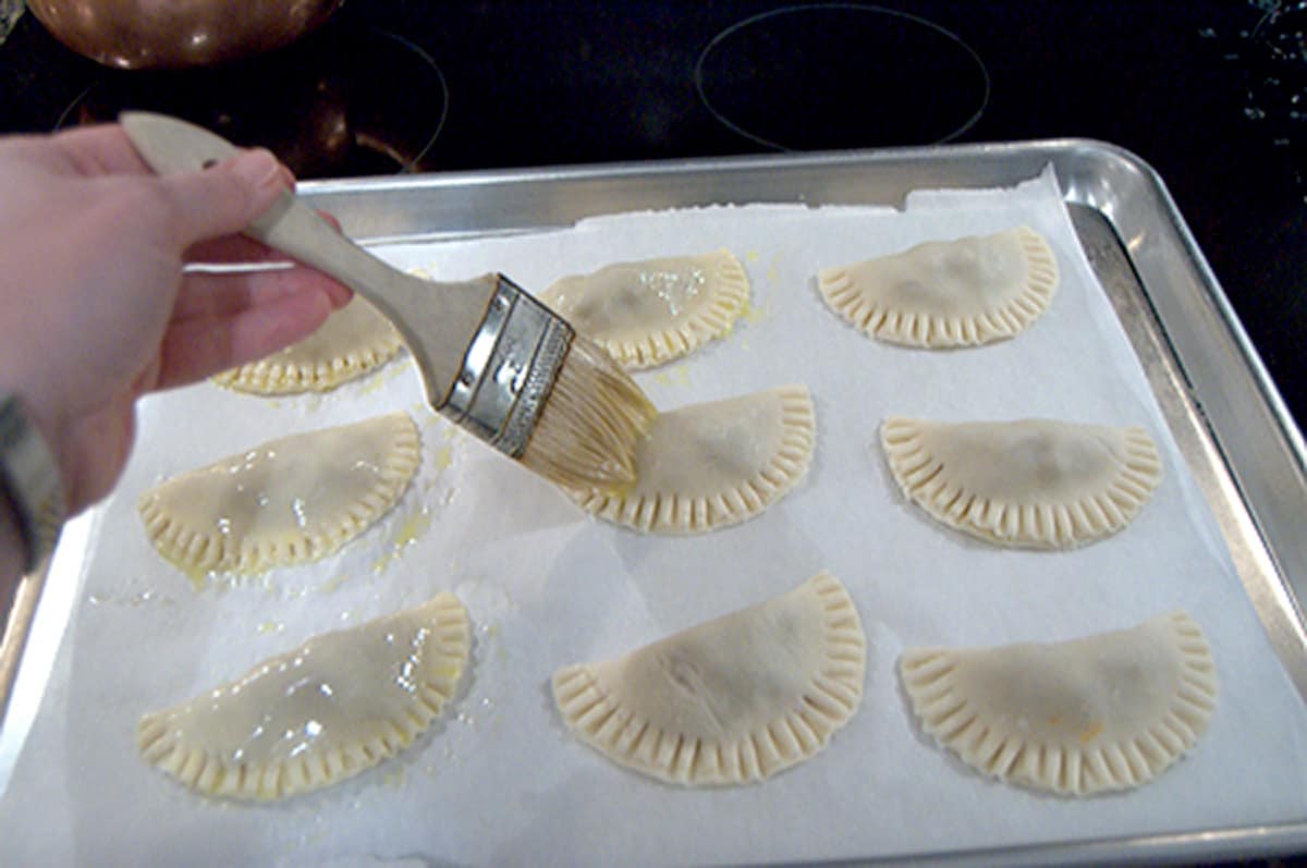 Prepared pies on a tray being brushed with egg white.