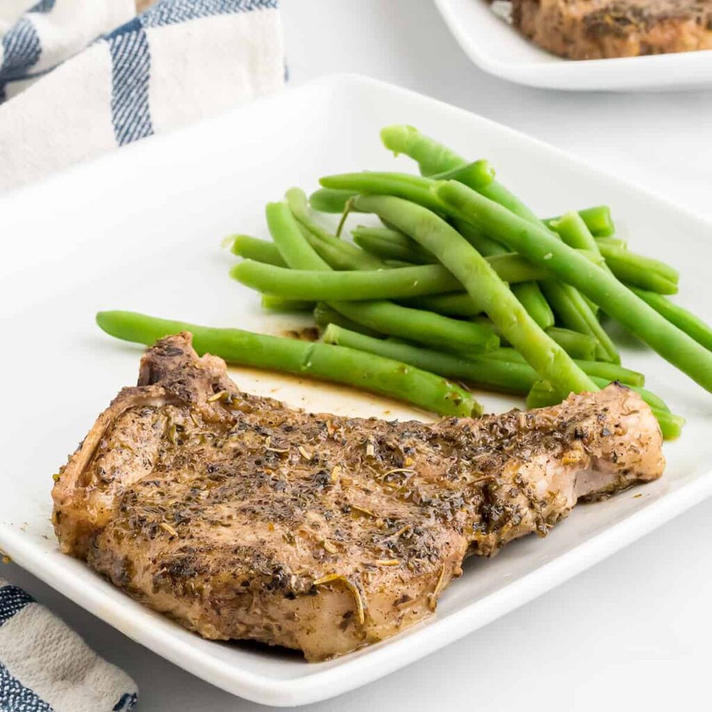 Finished pork chops and green beans on a white plate.