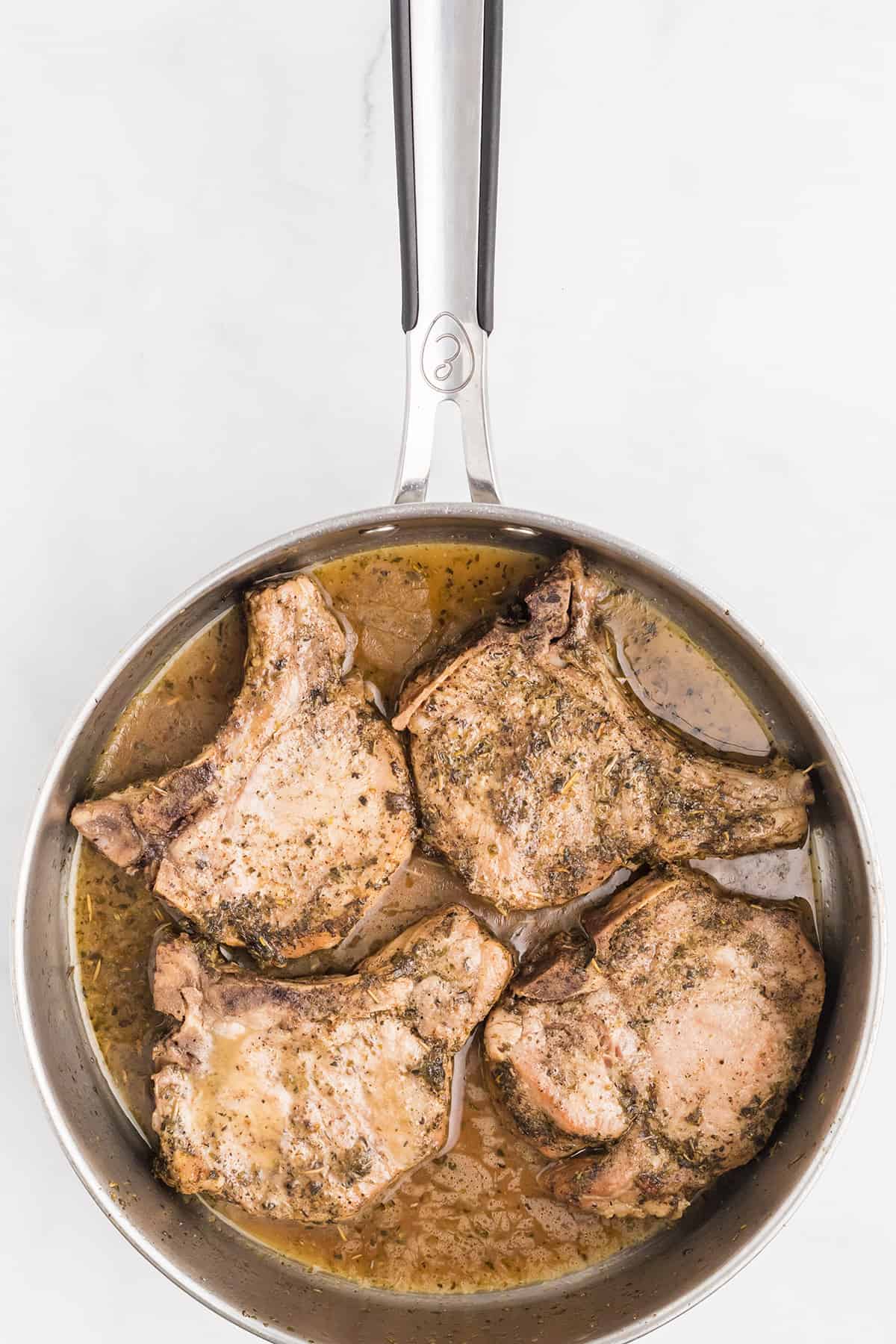 Chicken stock added to the pork chops in a skillet.