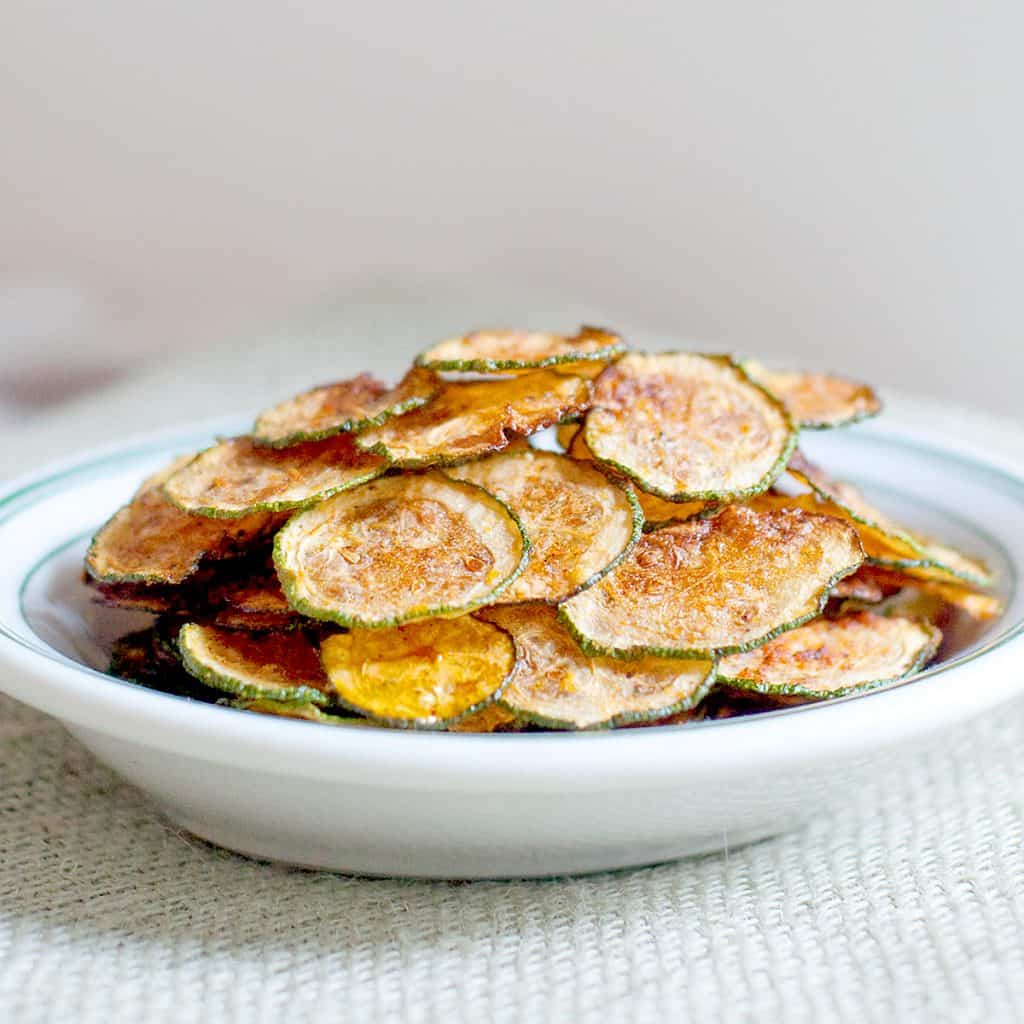 Baked zucchini chips stacked in a white bowl.