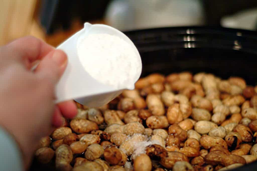 Adding salt to the peanuts in the crockpot.