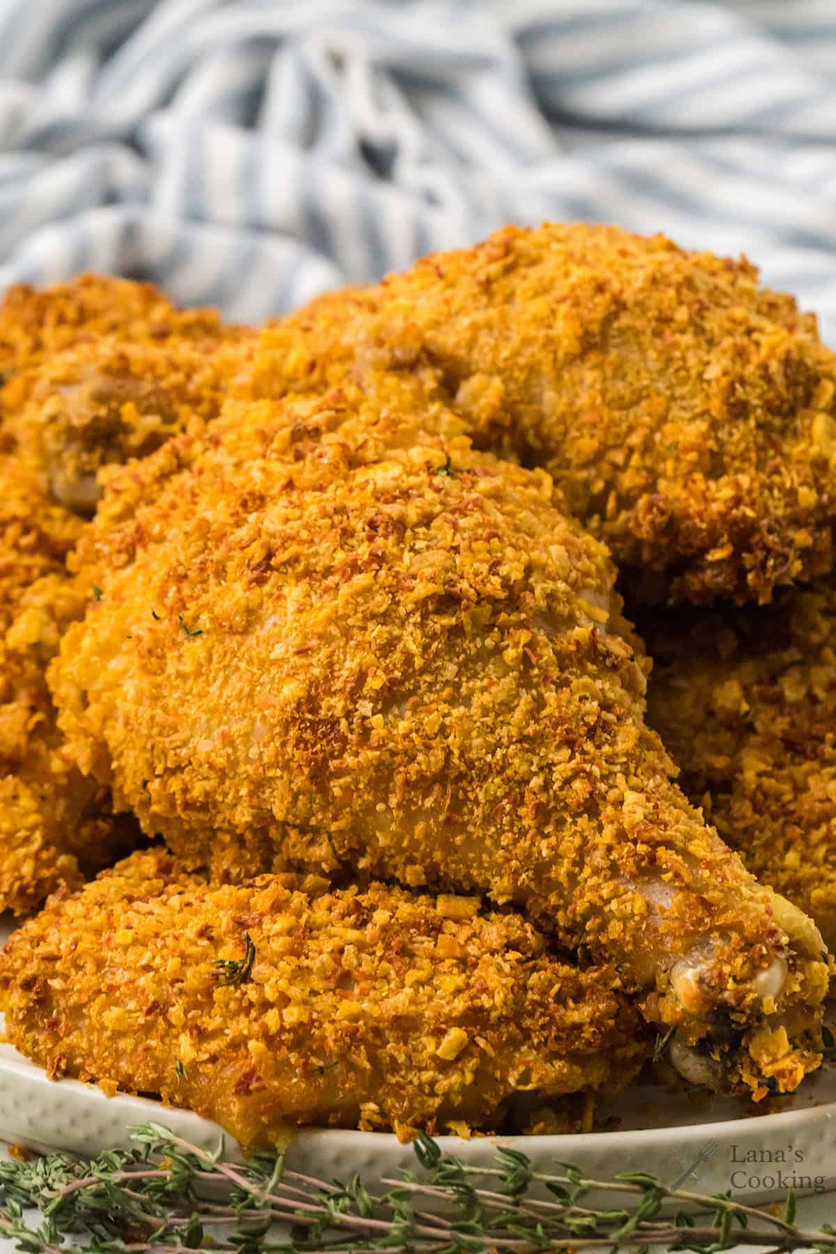 Crispy baked chicken drumsticks coated in a golden, crunchy breading on a plate, with a striped cloth behind.