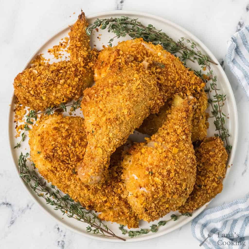 Plate of crispy baked chicken with a golden coating, garnished with fresh thyme sprigs on a marble surface.