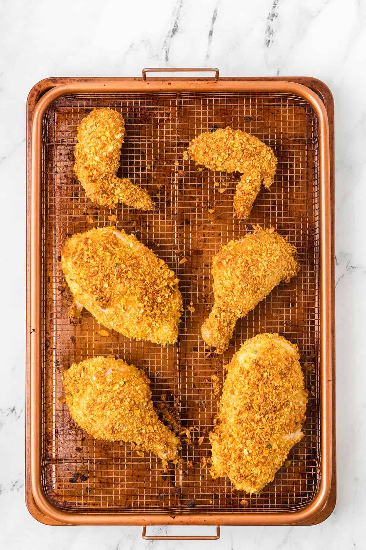Six pieces of breaded baked chicken on a wire rack over a baking sheet on a marble surface.