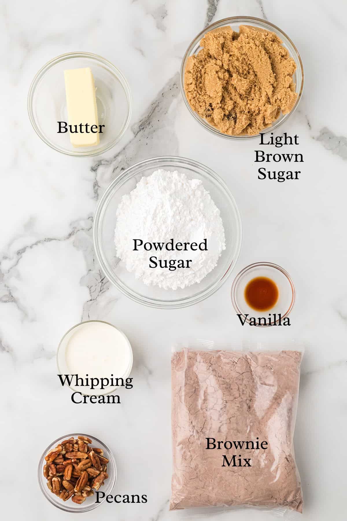 Ingredients on a marble surface: butter, light brown sugar, powdered sugar, vanilla, whipping cream, pecans, brownie mix.