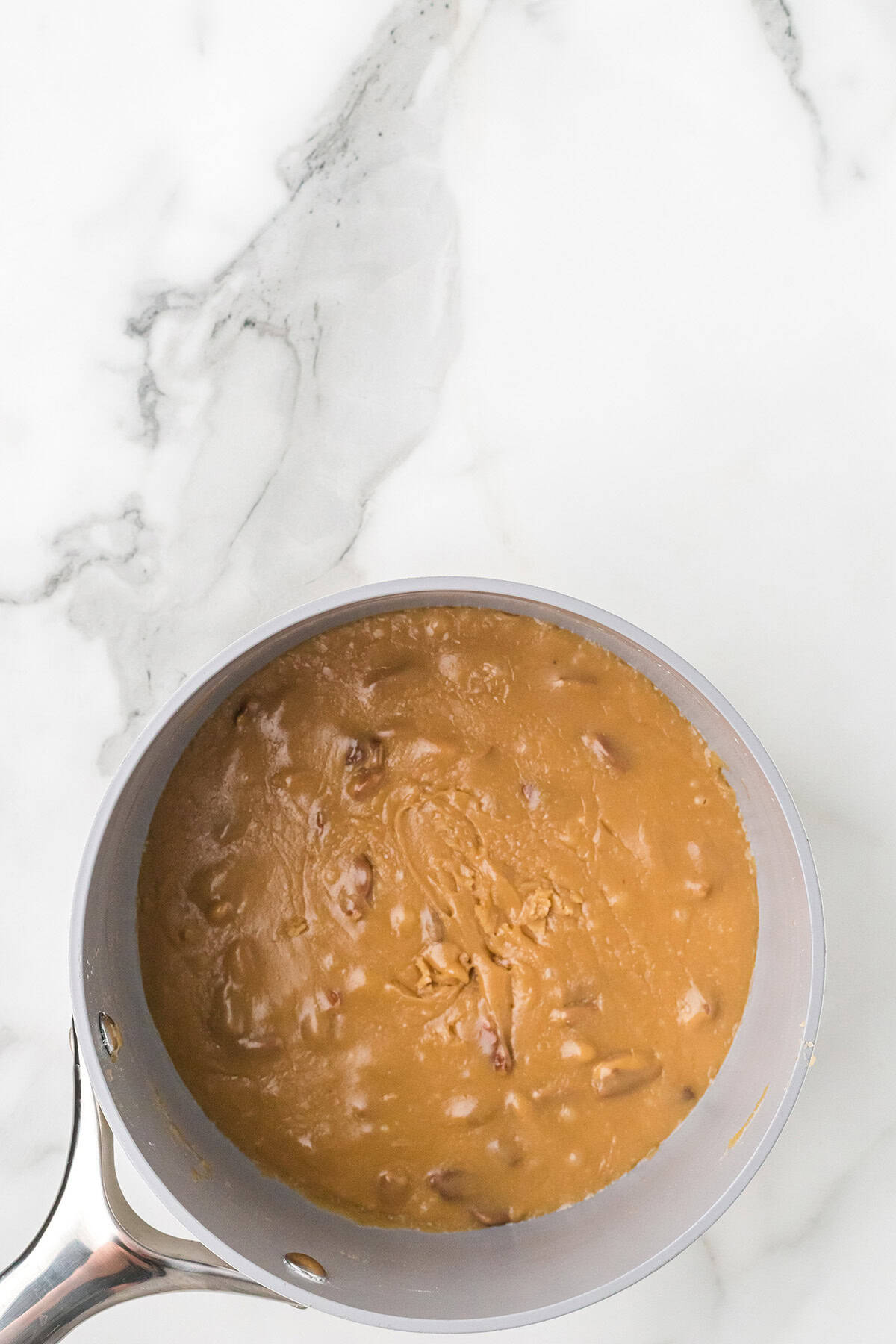 A saucepan filled with thick, brown caramel mixture on a white marble surface.