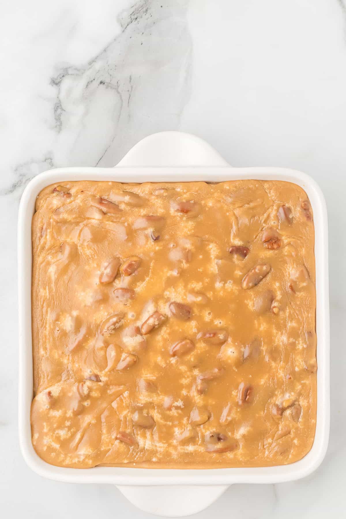 Square dish filled with praline topped brownies on a marble surface, viewed from above.