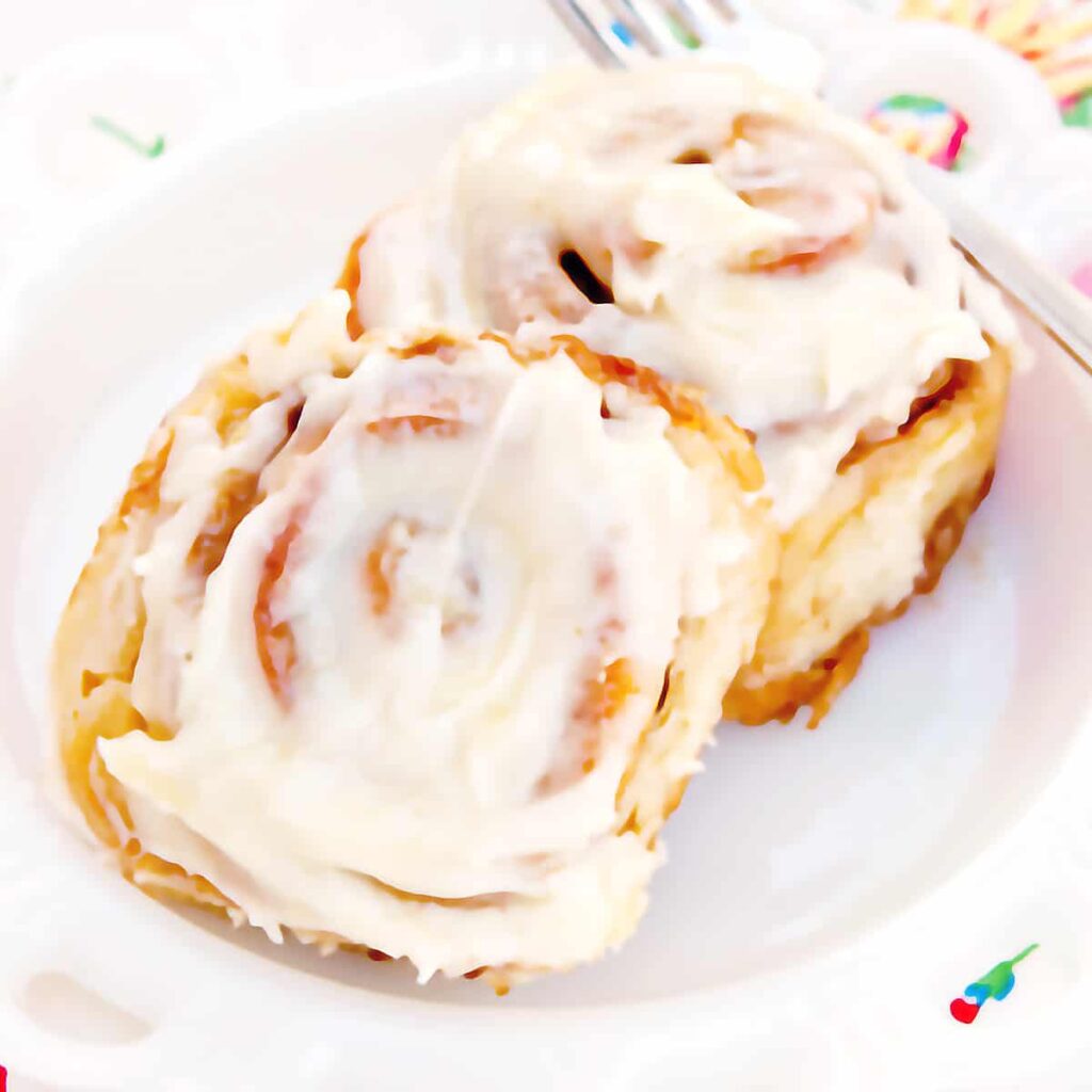 Two cinnamon rolls on a serving plate with a fork on the side.