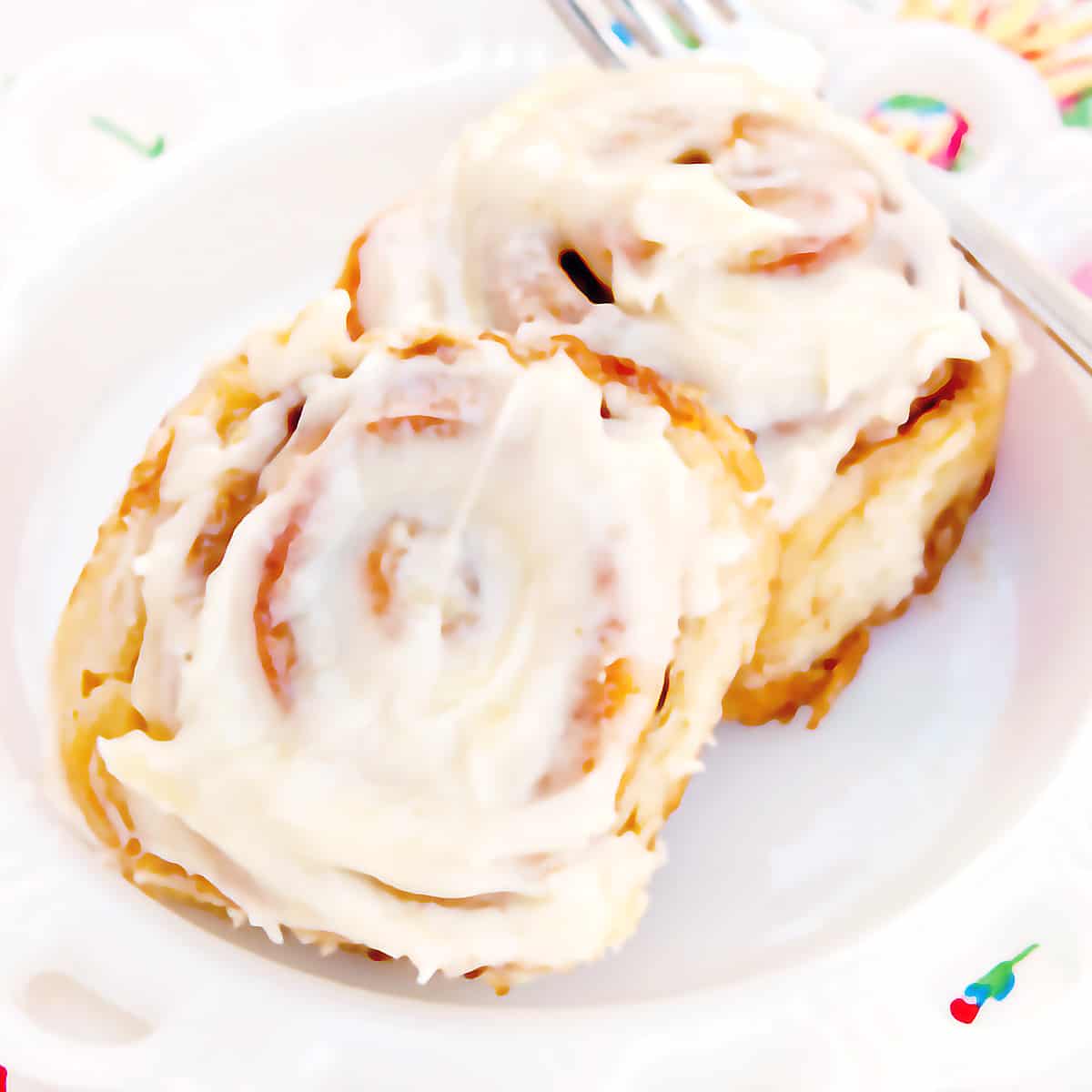 Two cinnamon rolls on a serving plate with a fork on the side.